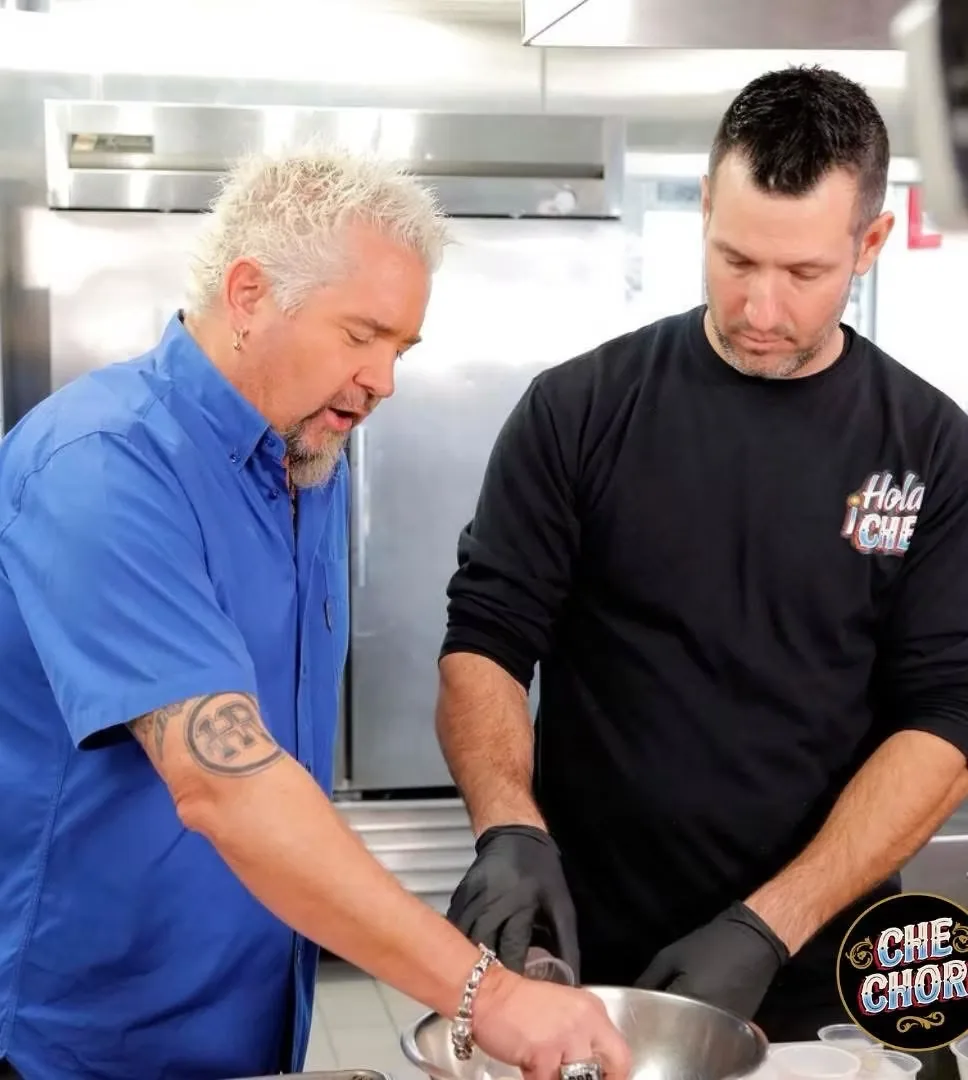 Guy Fieri and Chechori making empanadas together at a stainless-steel prep table in the café kitchen