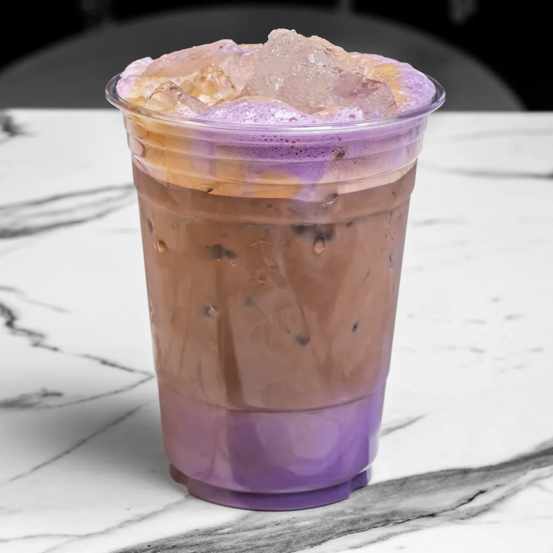 The Dreamer ube latte, layered purple and cream over ice, in a clear plastic cup on a white marble table