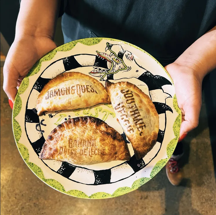 A plate of three freshly baked Chechori empanadas, each stamped with its flavor name, at Black House Café