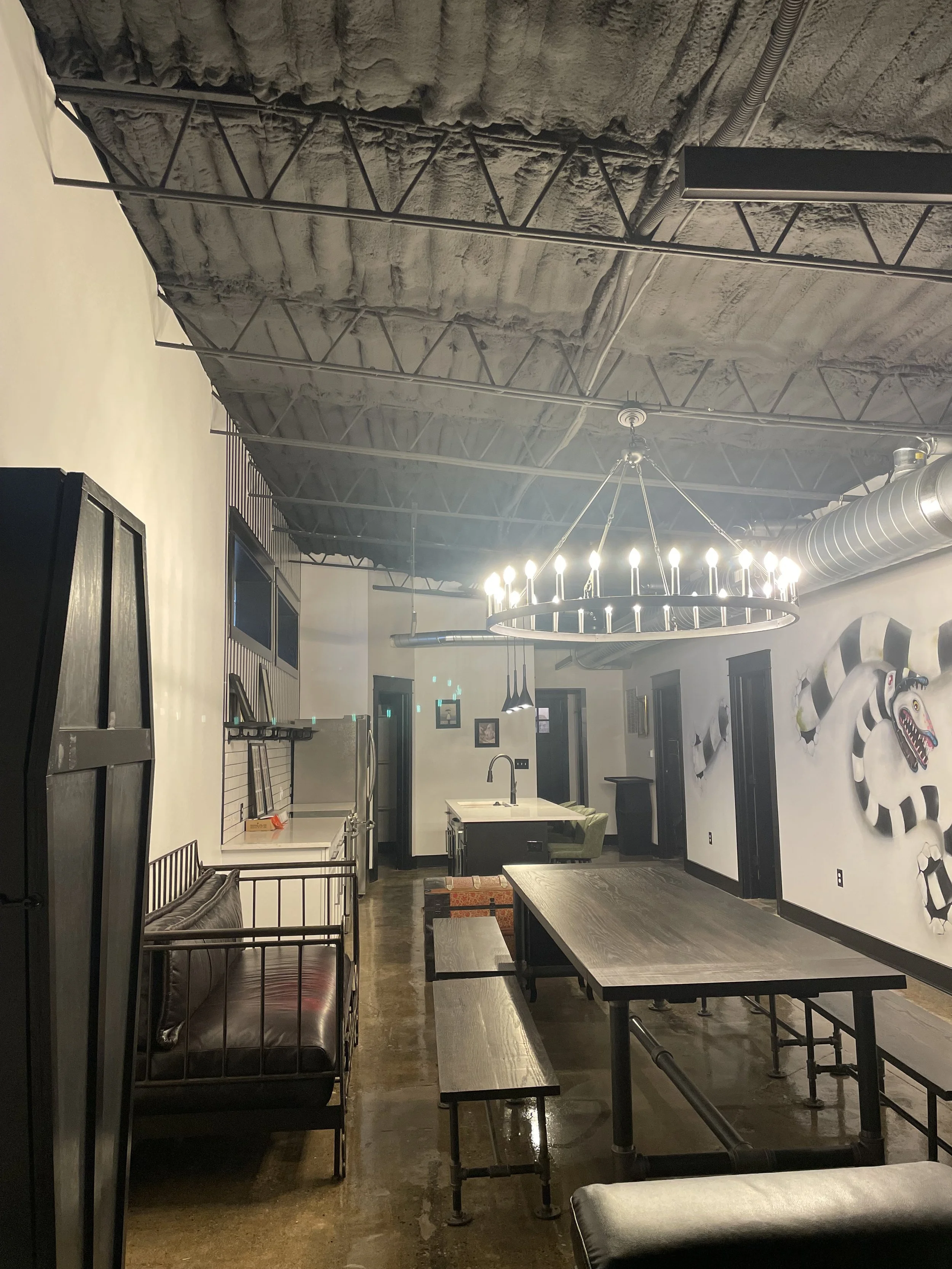 Interior event room at Black House Café with a long communal table, leather sofas, and a Beetlejuice sandworm mural, Indianapolis