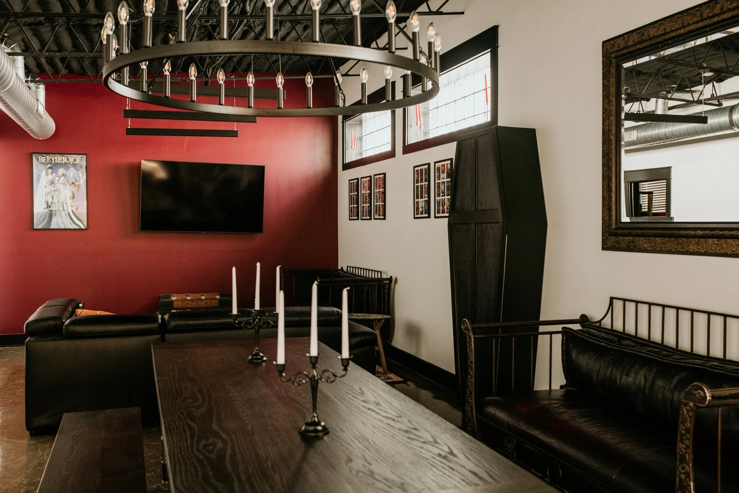 Interior event room at Black House Café with a red wall of framed horror memorabilia, a coffin cabinet, a wall-mounted TV, and a candelabra, Indianapolis