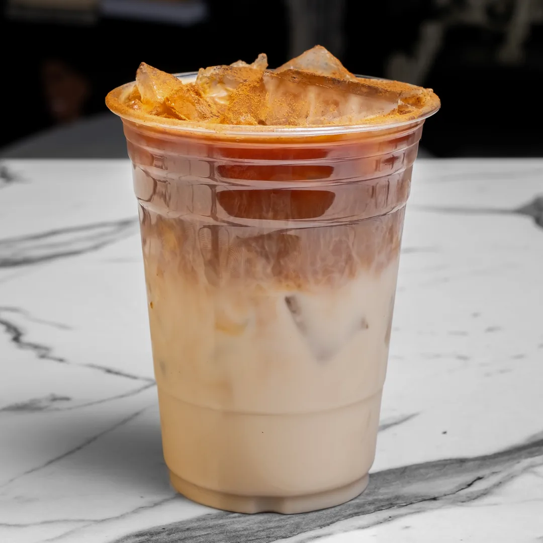 An iced horchata coffee latte dusted with cinnamon in a clear plastic cup on a white marble table