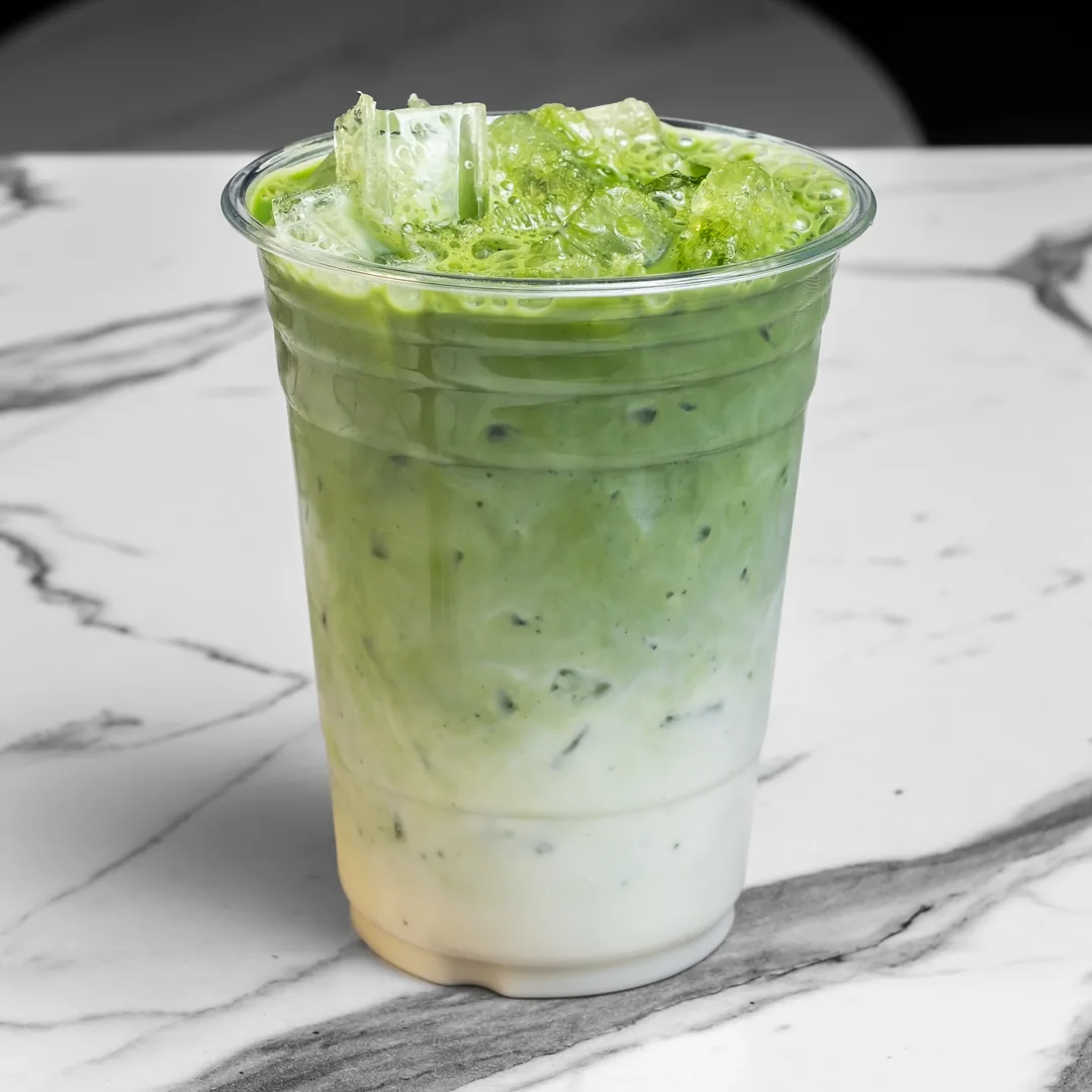 It's Alive pistachio matcha, bright green over ice, in a clear plastic cup on a white marble table