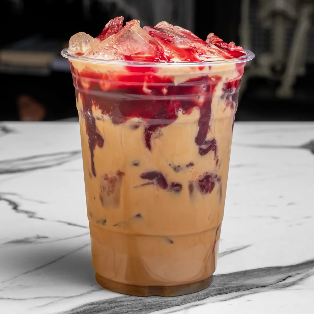 A raspberry white mocha with red raspberry syrup and ice in a clear plastic cup on a white marble table