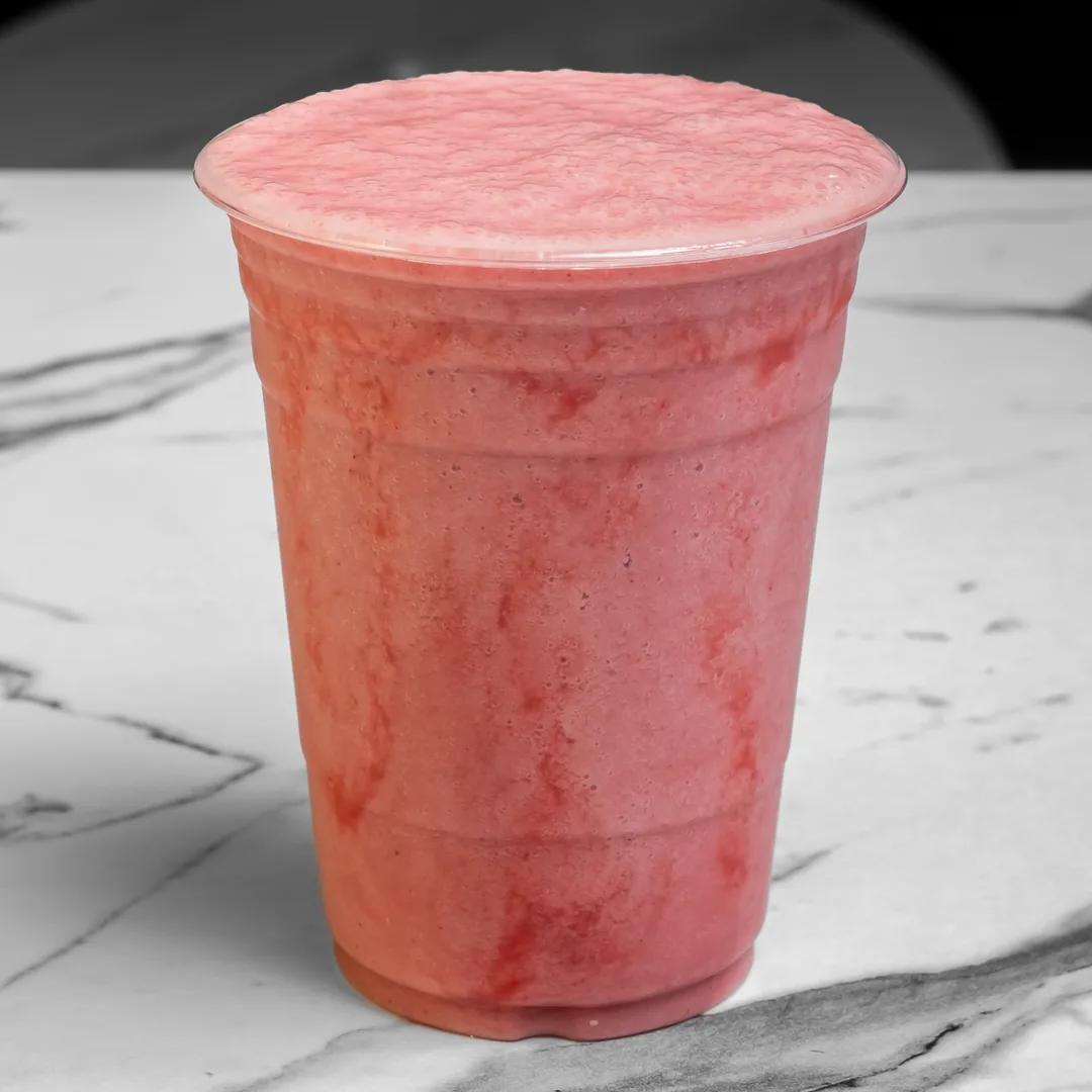 A pink strawberry banana smoothie in a clear plastic cup on a white marble table